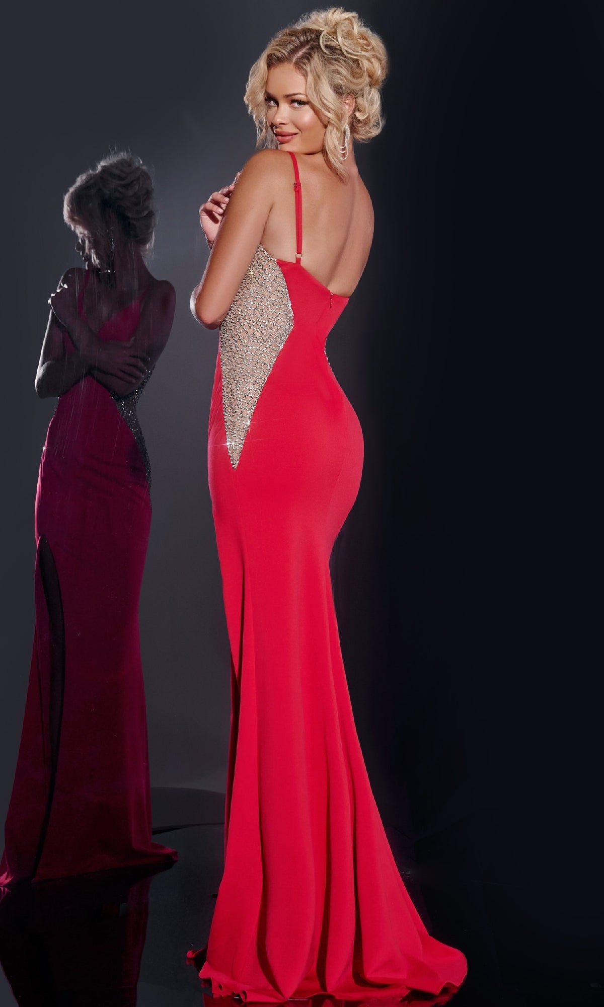Wearing the Long Prom Dress: Jovani 42002, which features silver side panels, a woman poses with her back to the camera beside a reflective surface that highlights her elegant profile.